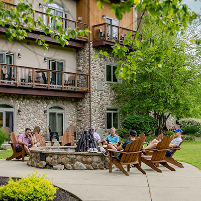 Guests sitting around a fire pit in the summer, outside of the Tamarack Club